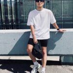 Man in white oversized t-shirt and black biker shorts leaning on concrete ledge
