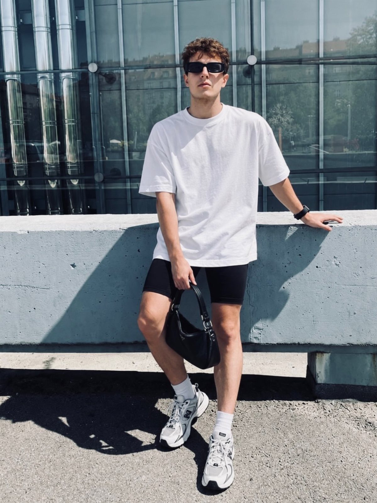 Man in white oversized t-shirt and black biker shorts leaning on concrete ledge
