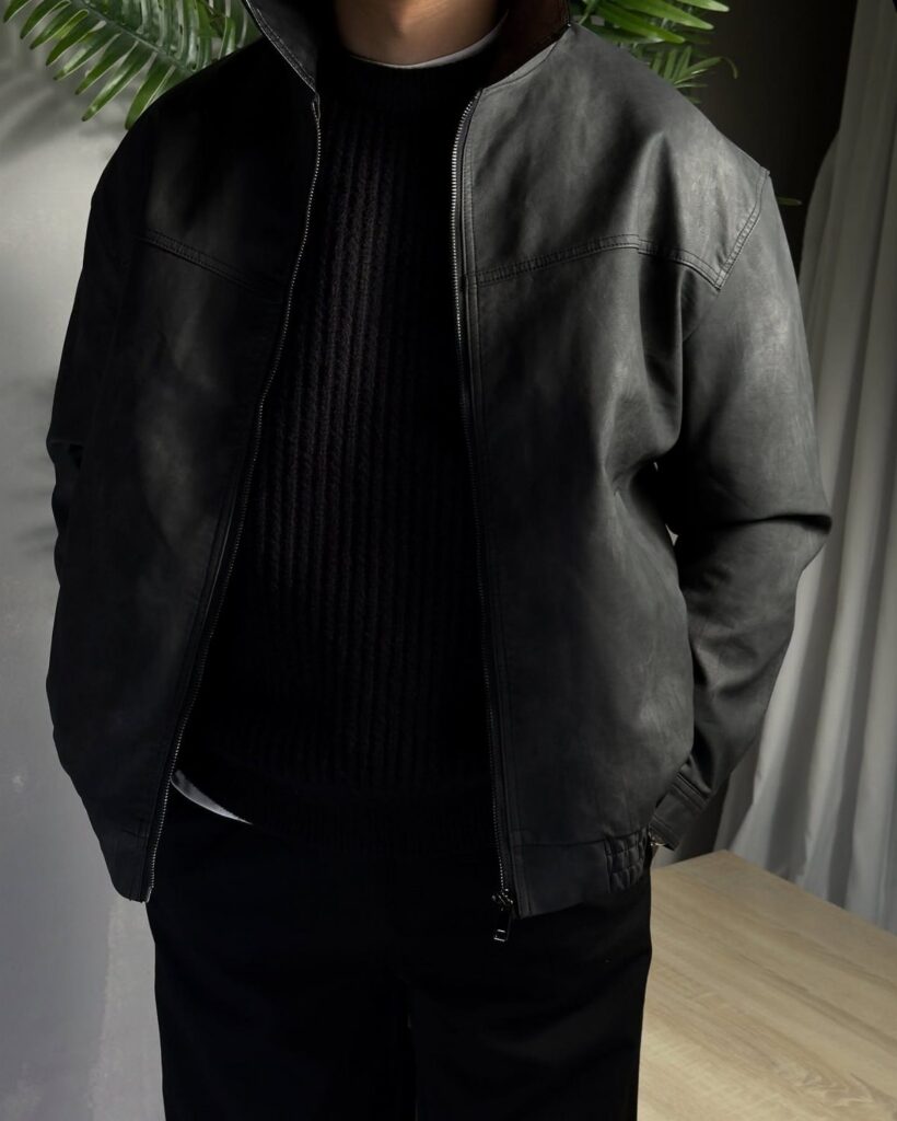 Person wearing a black ribbed sweater under a black leather jacket and trousers.