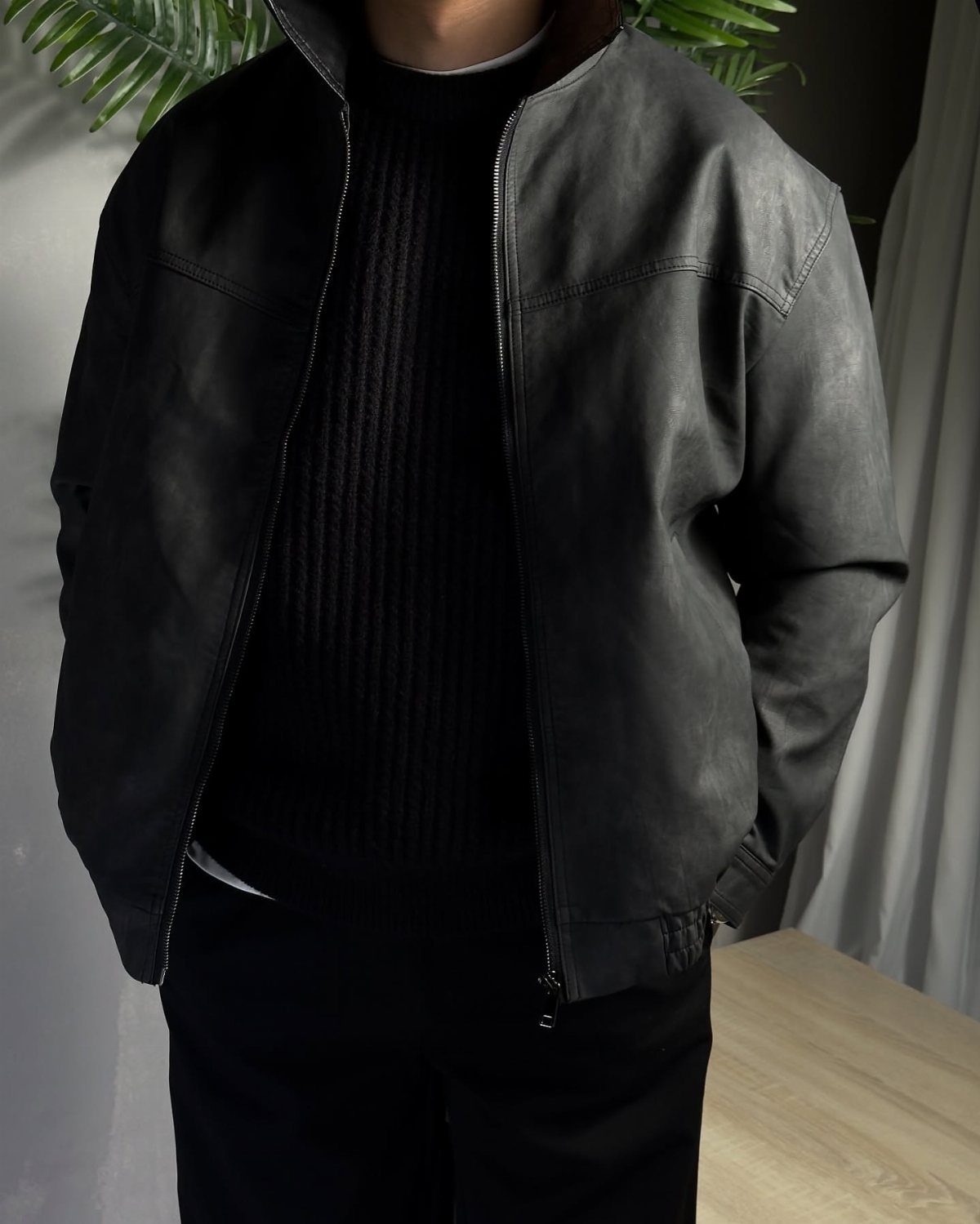 Person wearing a black ribbed sweater under a black leather jacket and trousers.