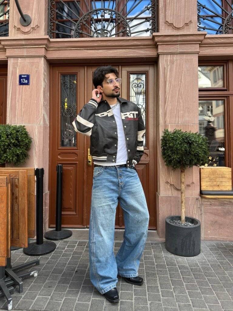 Man wearing a white t-shirt, varsity jacket, and light blue bootcut jeans.