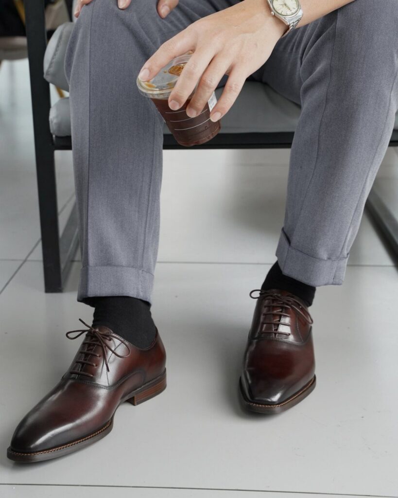 Dark brown leather dress shoes paired with grey trousers and black socks.