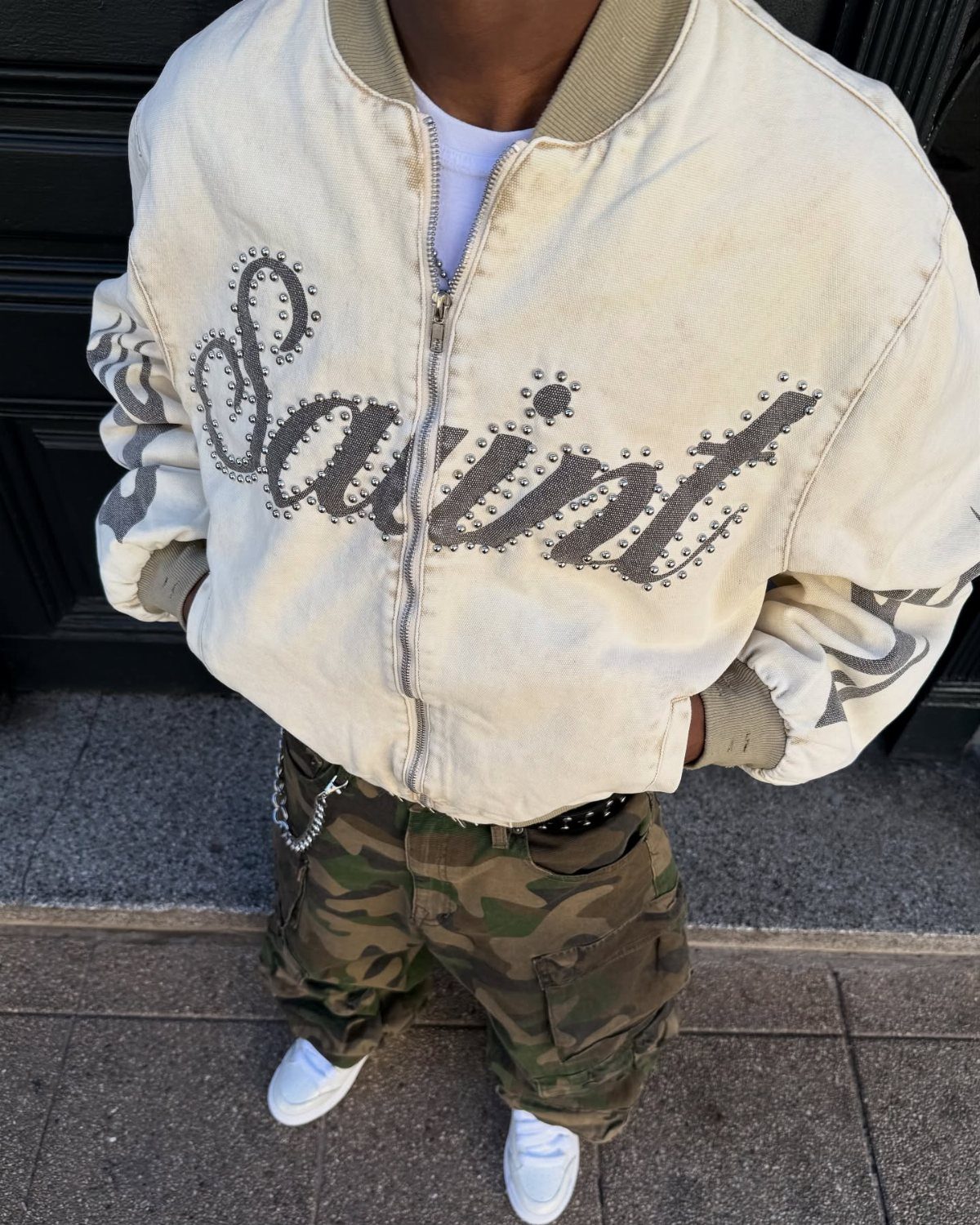 Person wearing a cream bomber jacket, green camo cargo pants, and white sneakers.