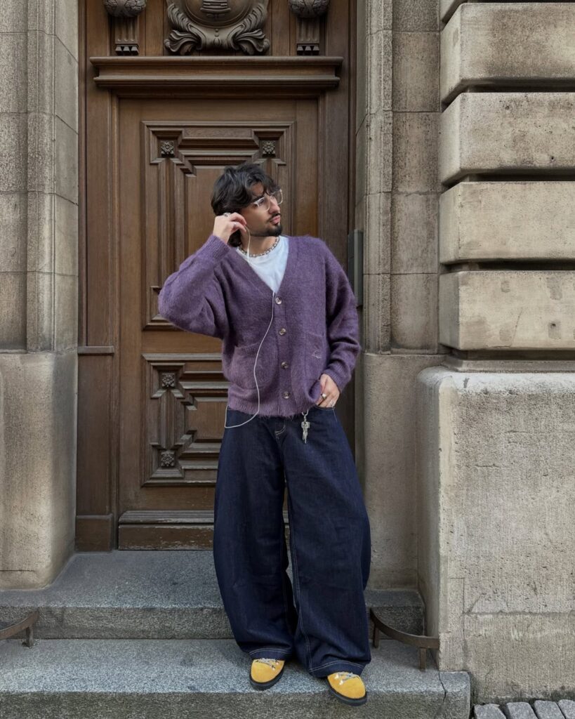 Man wearing a purple button-up cardigan and wide-leg dark blue jeans by a door.