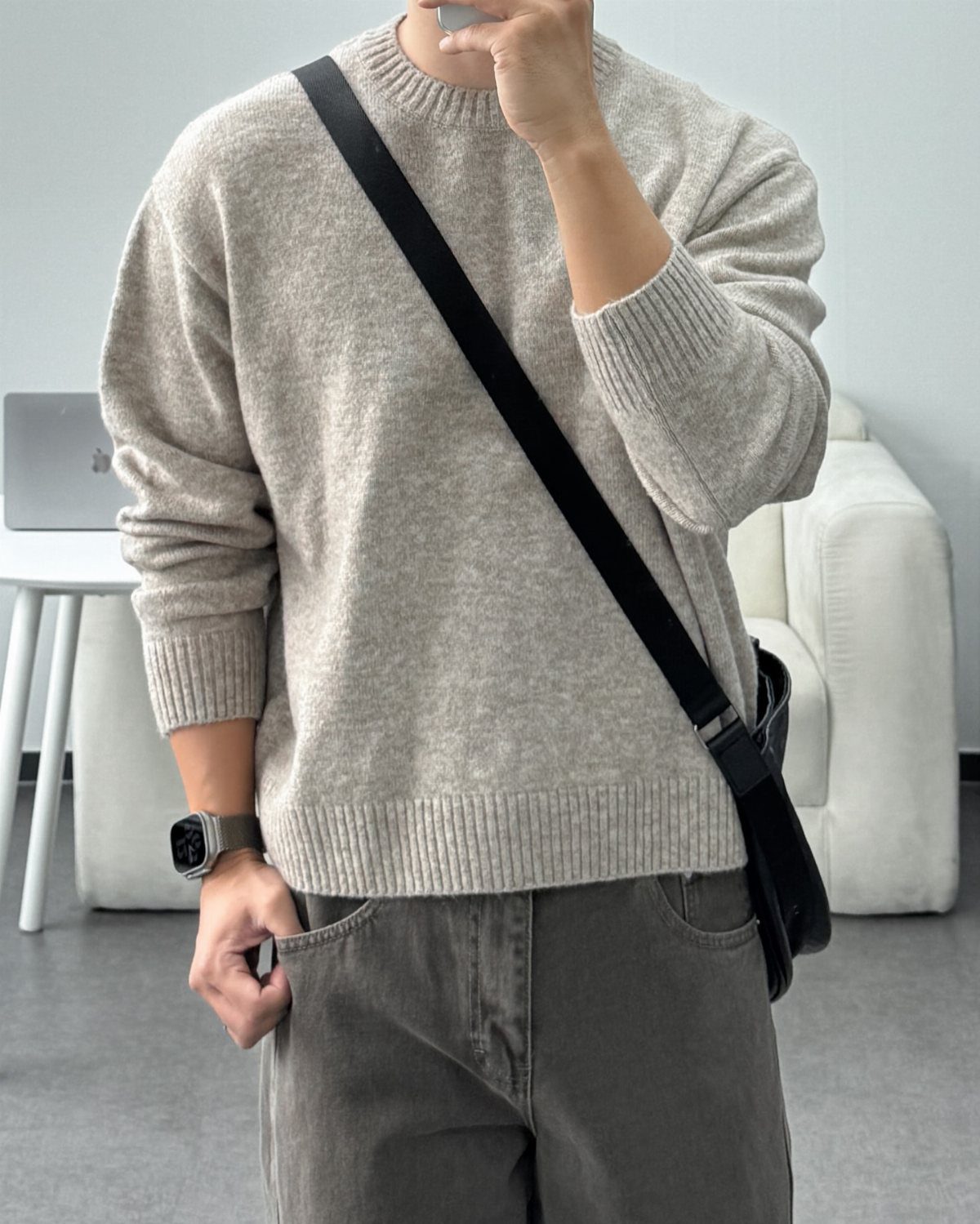 Person wearing a light beige cropped sweater with grey trousers and black crossbody bag.