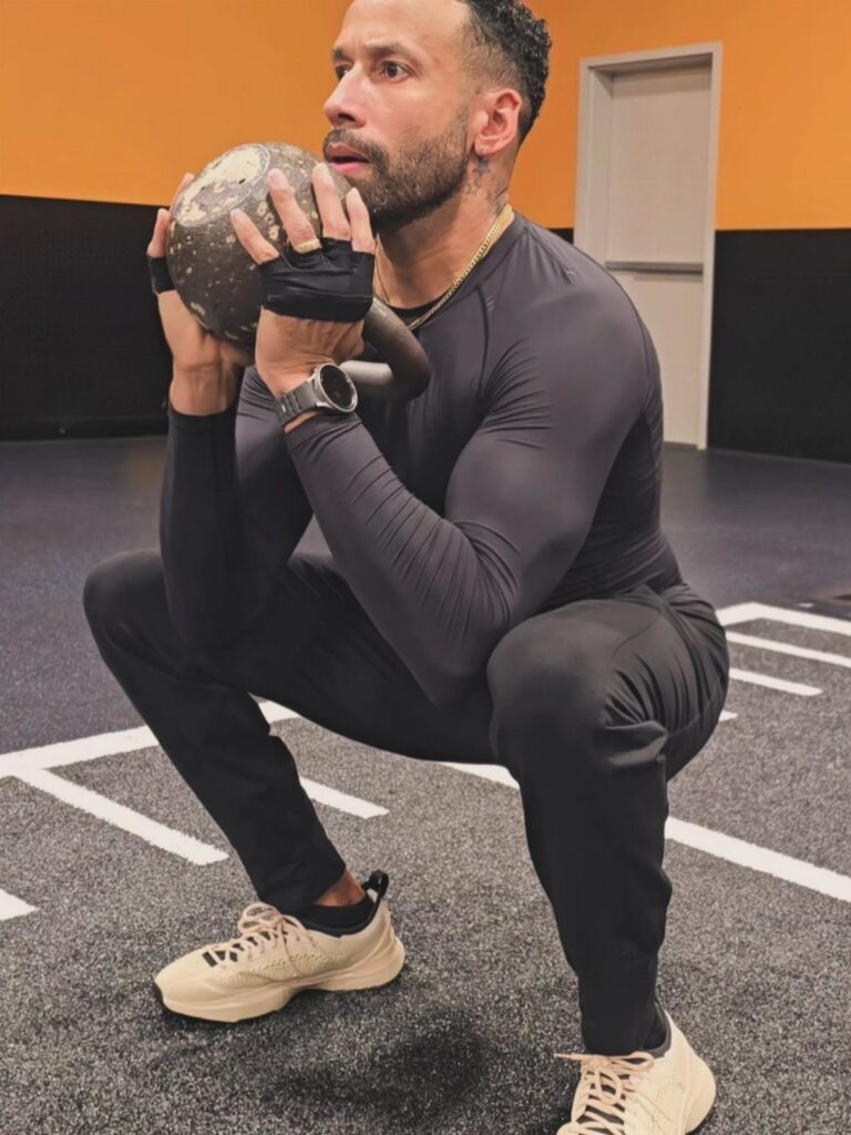 Man in tight black athletic wear holding a medicine ball in a gym