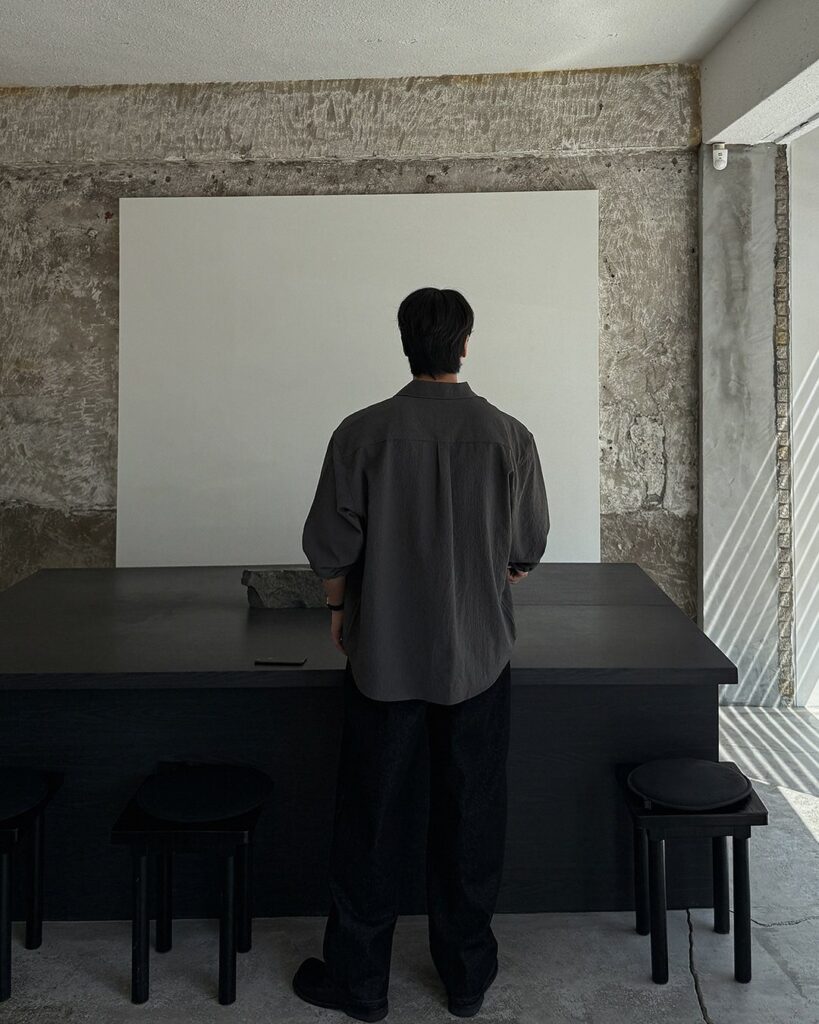 Man from behind wearing a gray shirt and black pants in minimalist studio