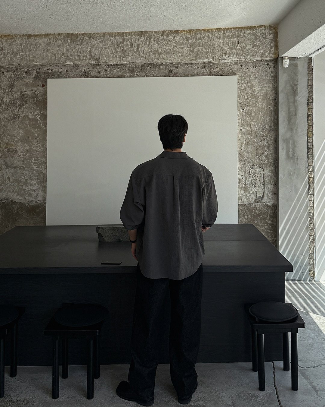 Man from behind wearing a gray shirt and black pants in minimalist studio