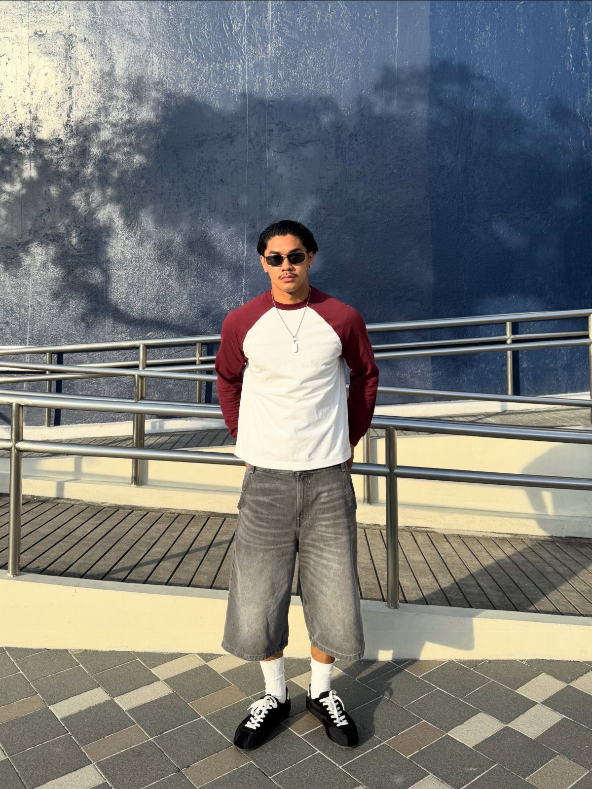 Man wearing a raglan shirt and wide-leg grey denim shorts with black sneakers.