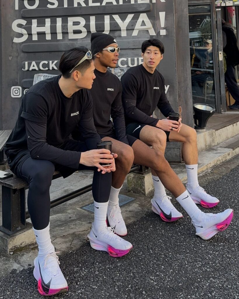 Three men in black athletic wear and white sneakers sitting on a bench.