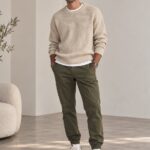Man wearing a beige sweater and olive green joggers with white sneakers.