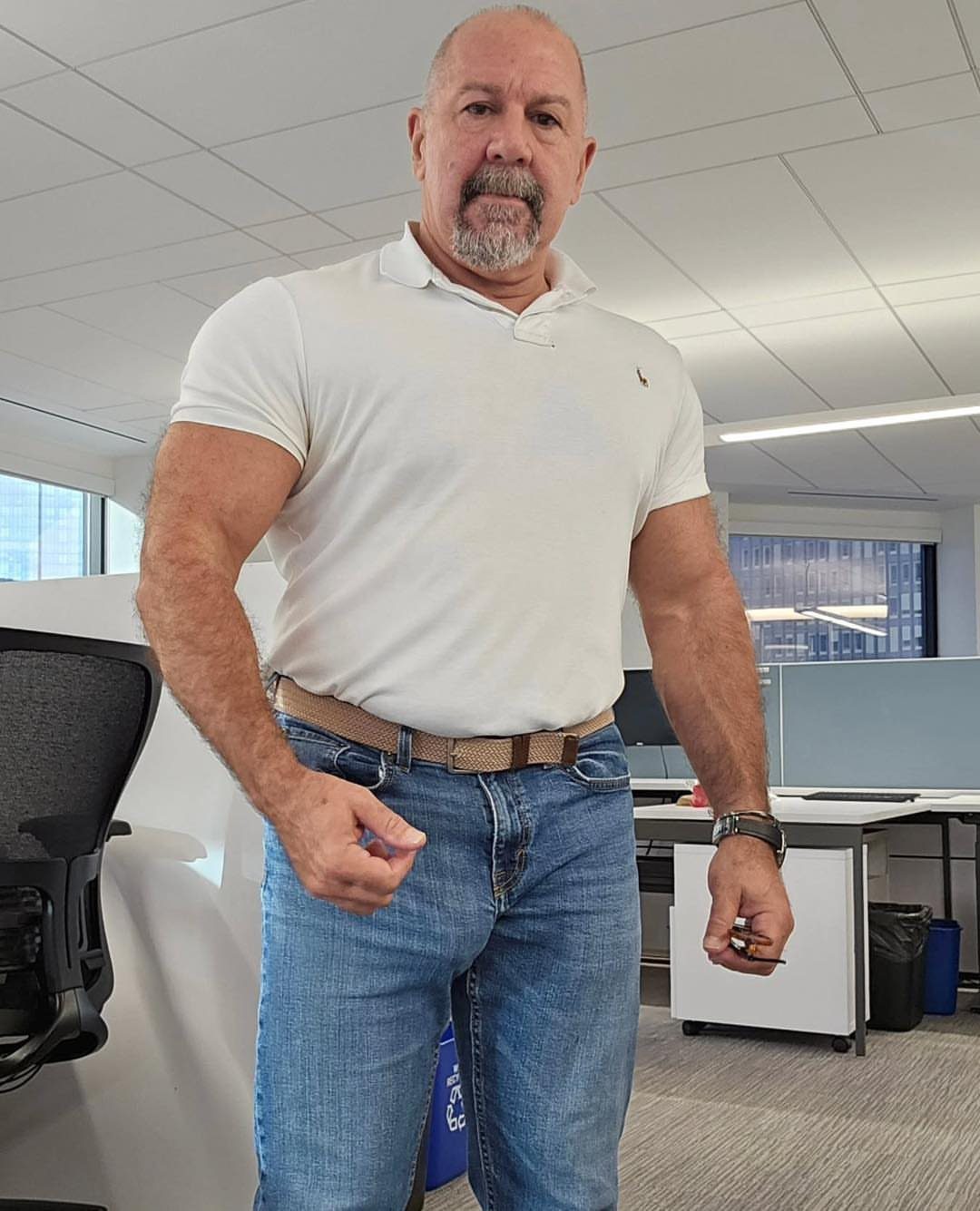 Muscular middle-aged man wearing a white polo shirt and blue jeans in an office.