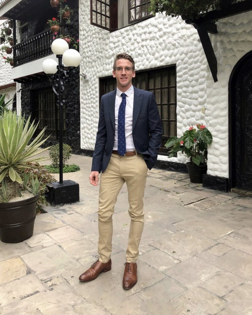 Man wearing a navy blue blazer and khaki pants standing in a courtyard
