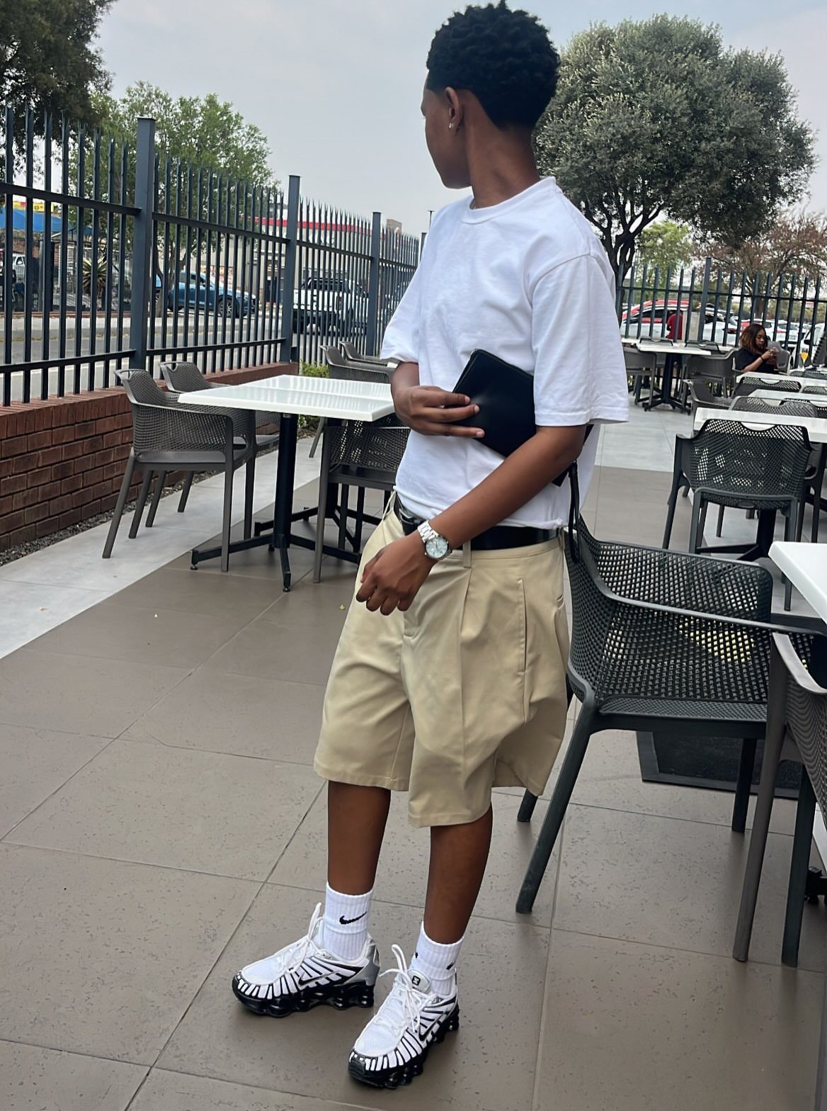 Person wearing a white t-shirt and pleated khaki shorts on an outdoor patio