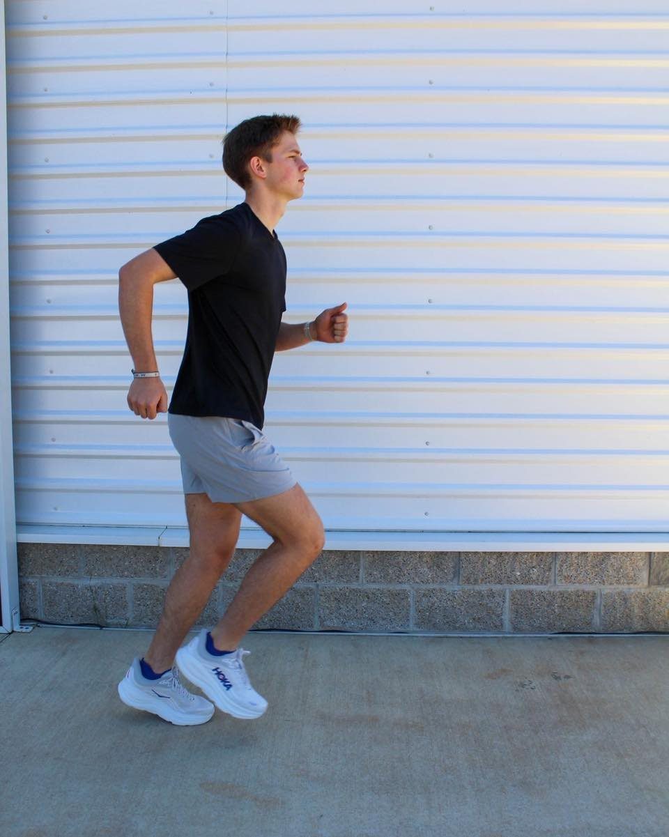 Man running in a black t-shirt and grey athletic shorts against a white wall