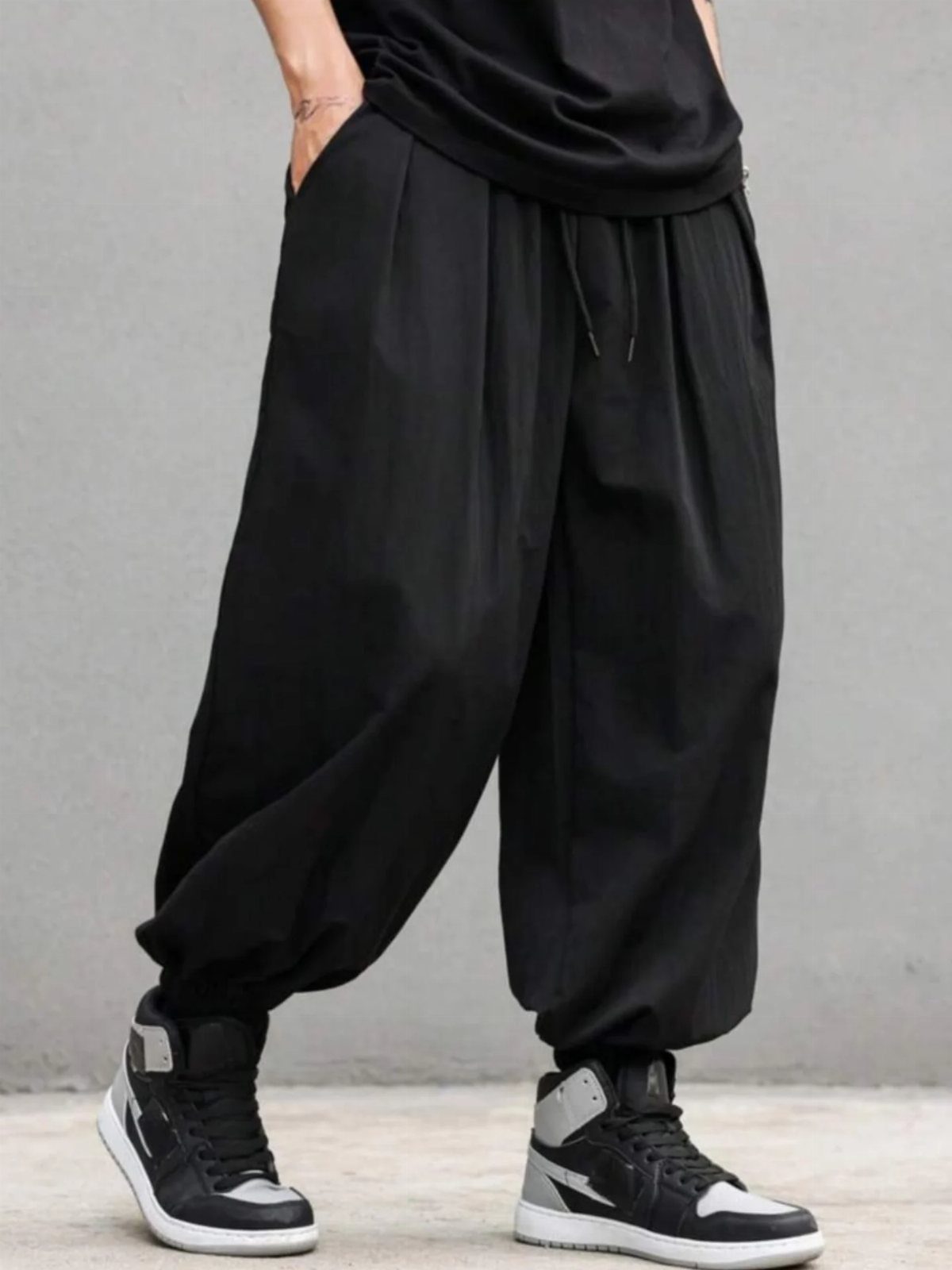 Oversized black joggers with drawstring waist and high-top sneakers against grey wall