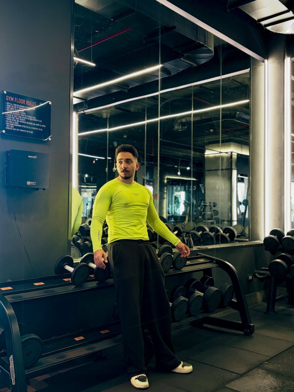 Man in neon yellow long-sleeved shirt and black pants posing in a gym.