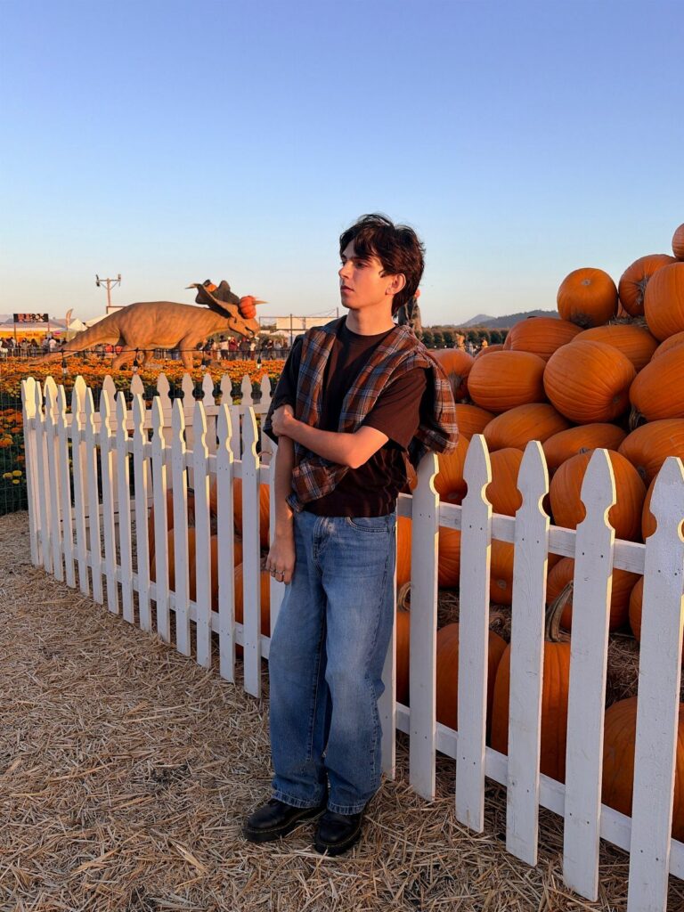 Teenage boy wearing a burnt orange plaid shirt over a dark tee and jeans.