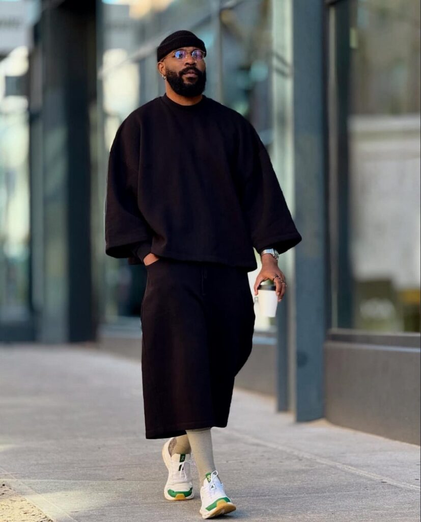 Man in oversized black t-shirt and long black shorts walking on city sidewalk