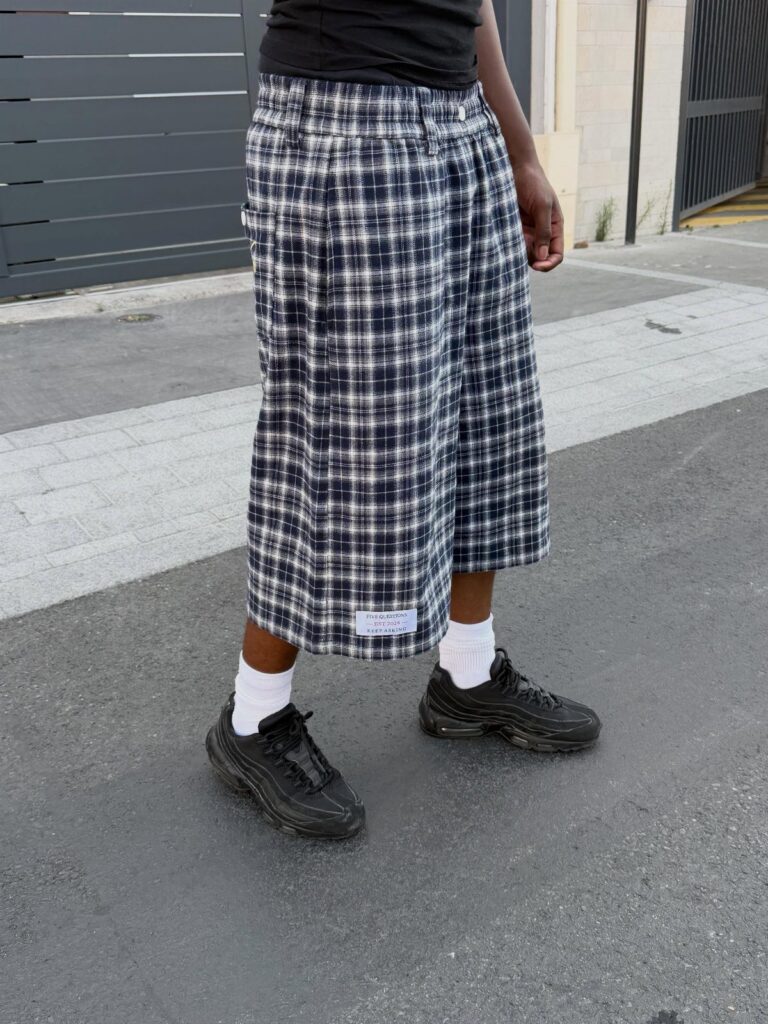 Person wearing navy and white plaid wide-leg shorts with black sneakers and white socks.