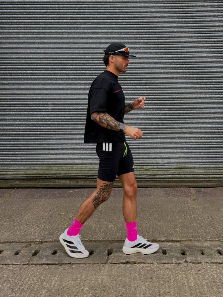 Man walking in black athletic shorts, black t-shirt, and bright pink socks.