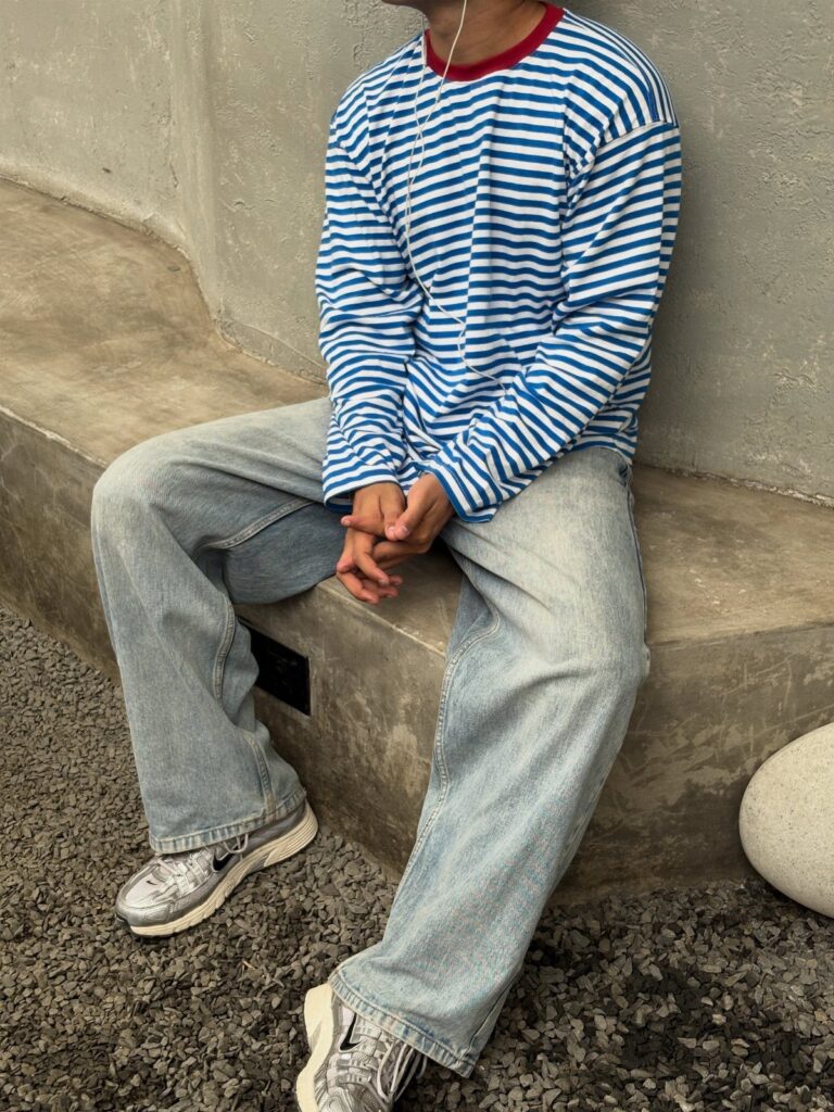Person wearing a blue and white striped t-shirt with light blue jeans sitting outdoors.