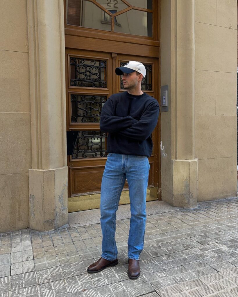 Man wearing slim straight blue jeans, black shirt, and brown leather shoes.