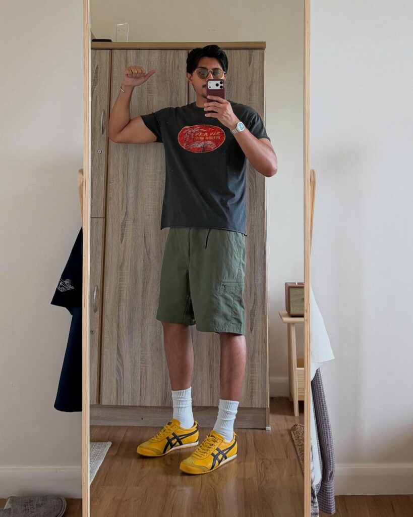 Man in grey graphic tee, olive cargo shorts, and yellow sneakers posing in mirror.