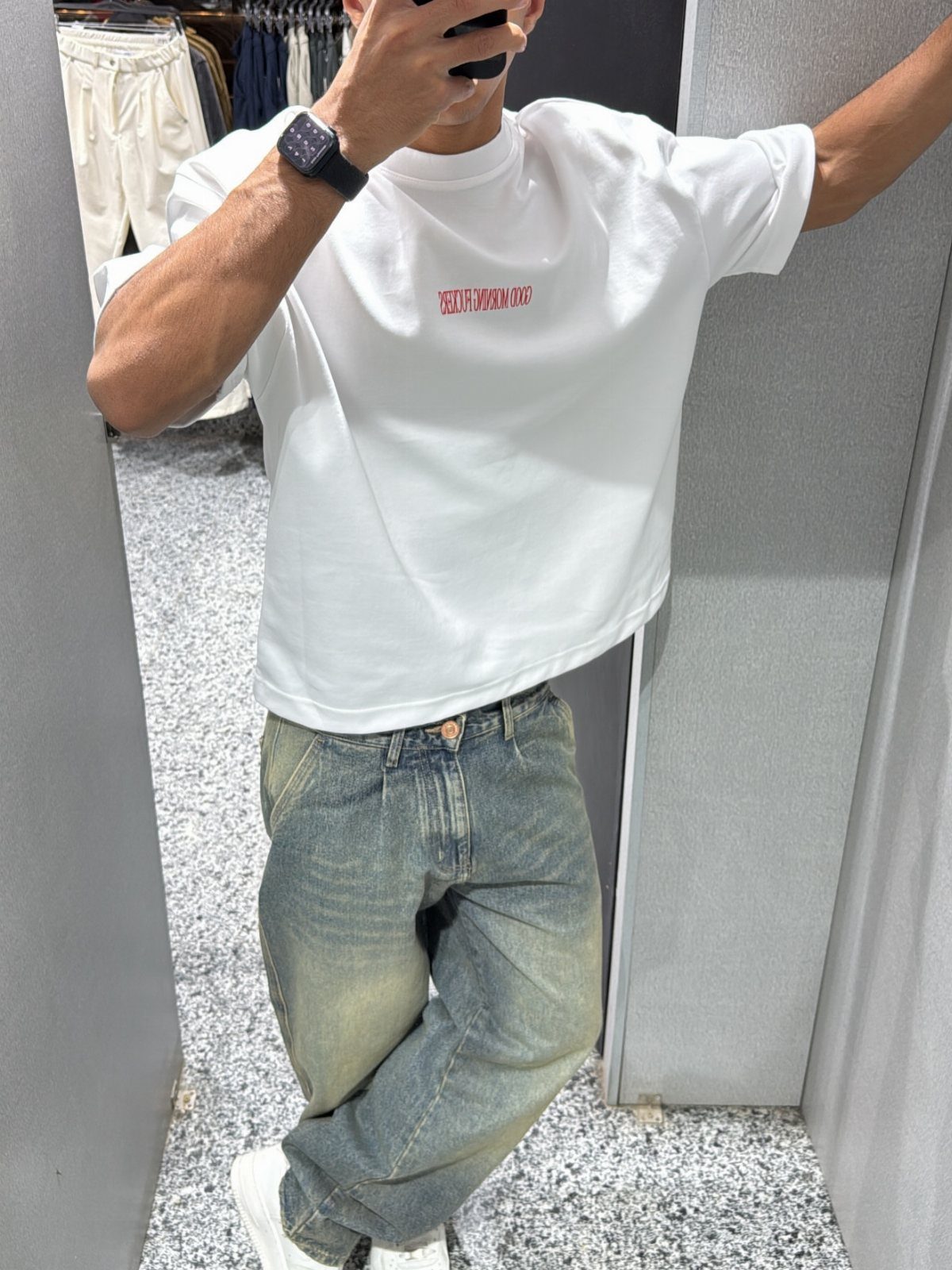 Person wearing a white logo t-shirt and faded blue jeans in a store.